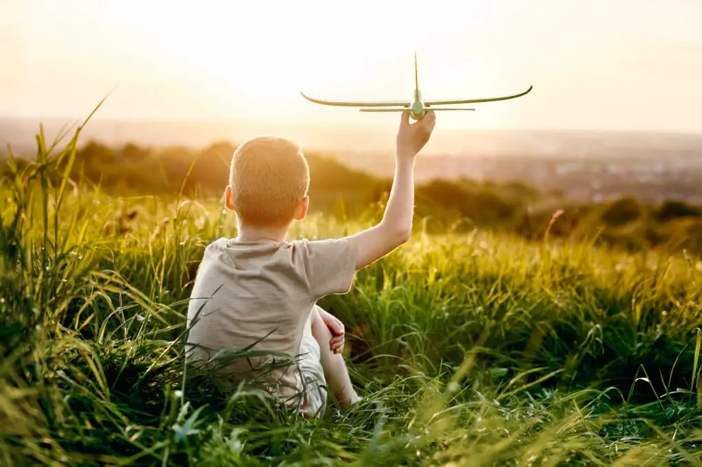 Little boy sitting on the meadow with toy airplane